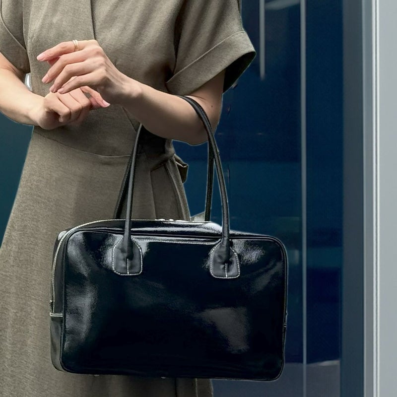 カーキのワンピースの女性が、黒いエナメルのボストンを手に提げている